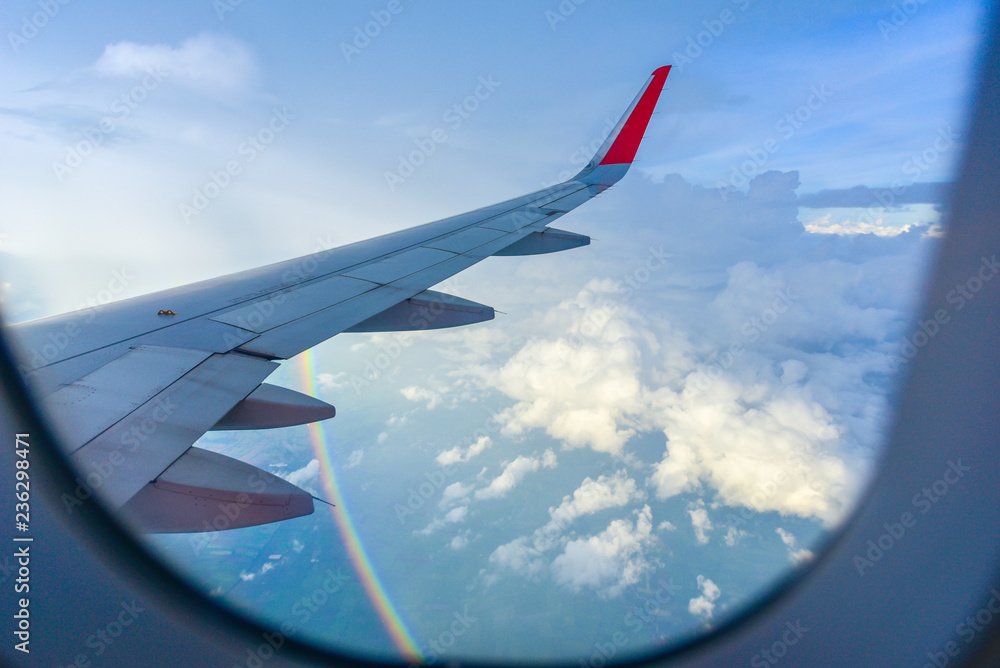 一架在云层上方飞行的飞机的机翼。从机舱窗户看彩虹。