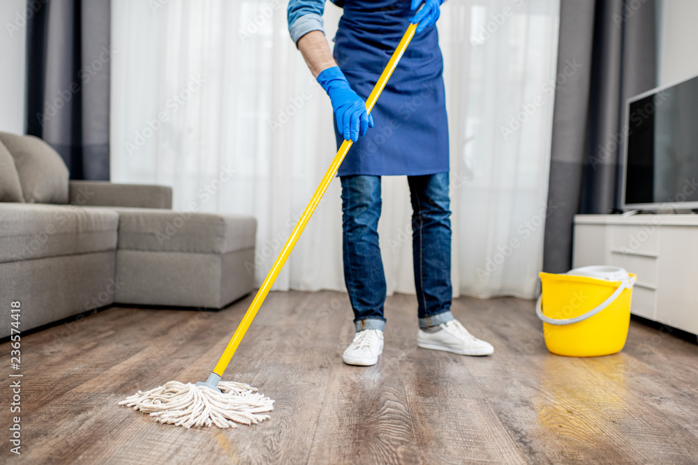 一名身穿蓝色制服的专业清洁工在客厅里用拖把和水桶洗地板