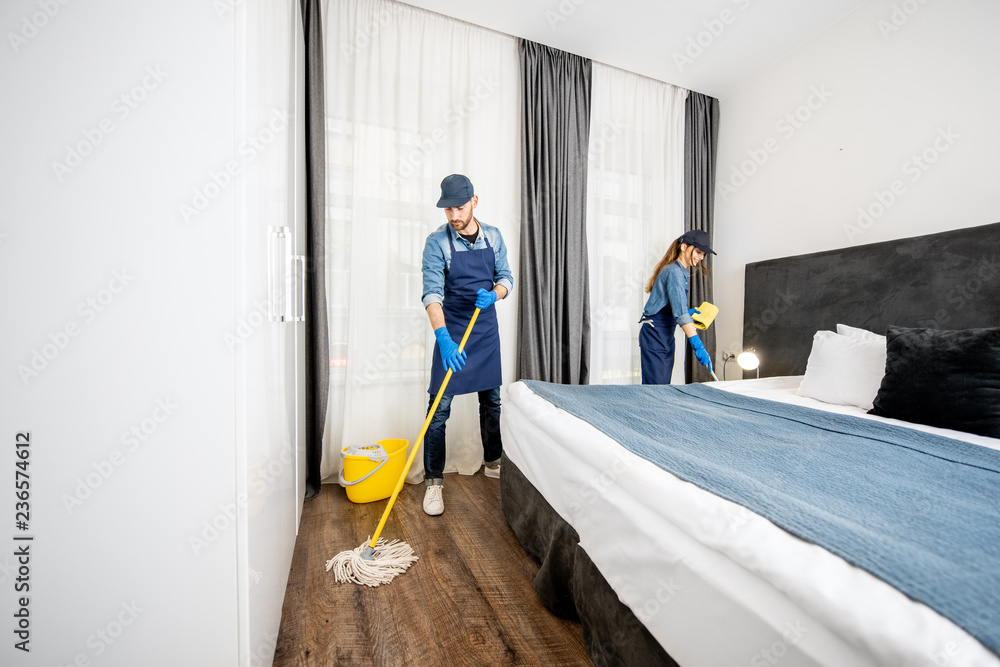穿着制服的专业清洁工在酒店房间里洗地板，擦家具上的灰尘
