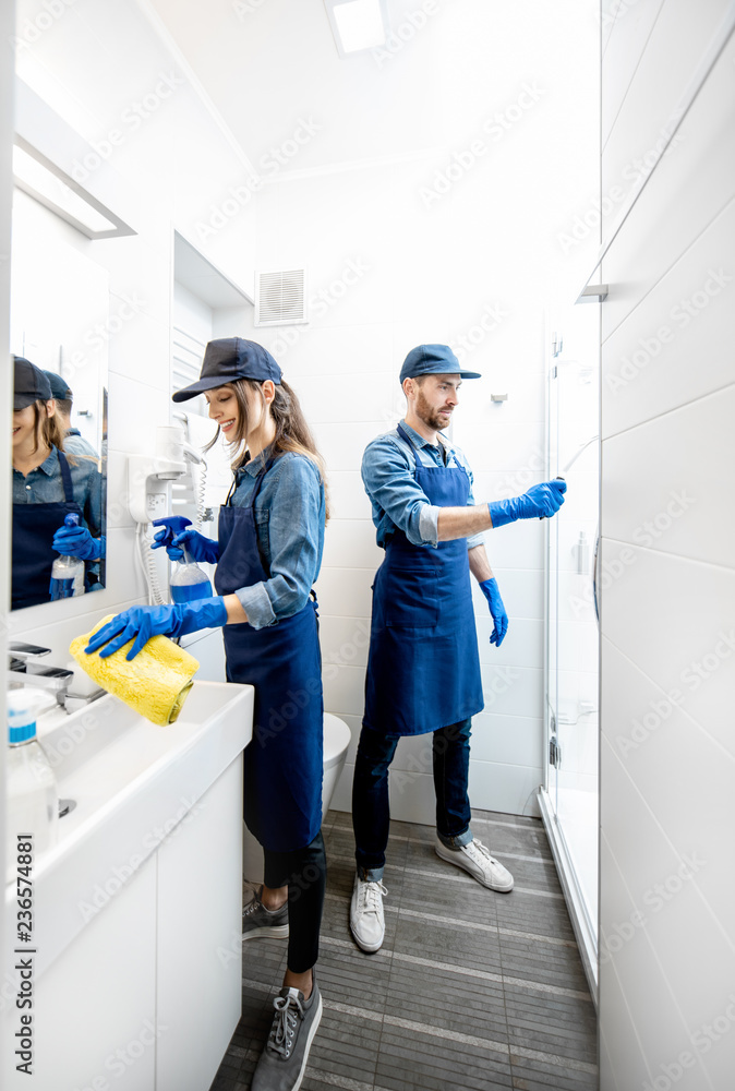 情侣作为专业清洁员，穿着蓝色制服清洁浴室。清洁服务理念