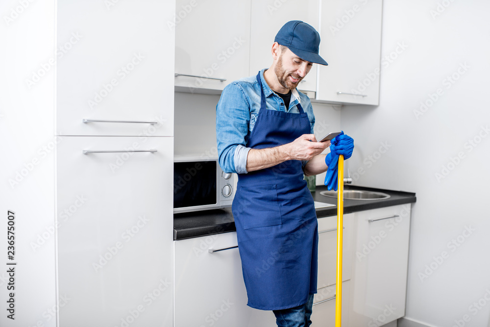 Man as a professional cleaner standing with phone having a break during the work on the kitchen