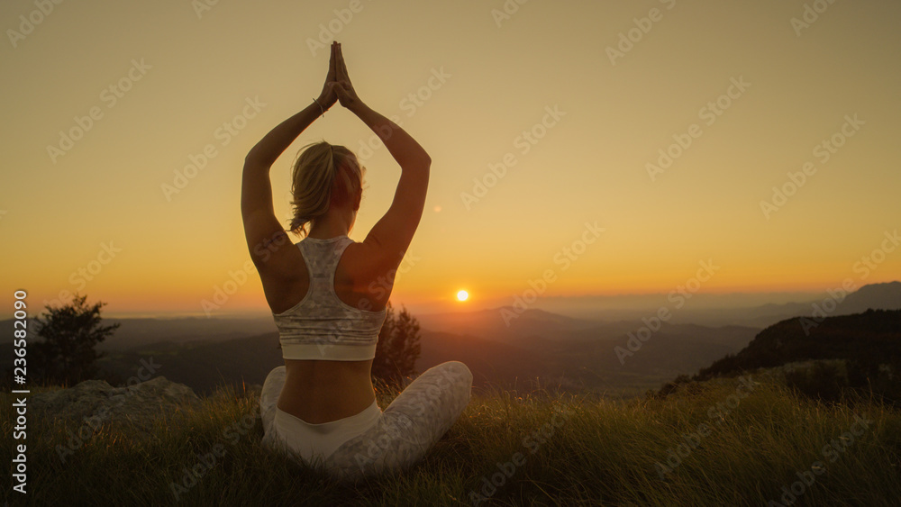特写：一个阳光明媚的夏日夜晚，一位活跃的女士在山上做瑜伽。