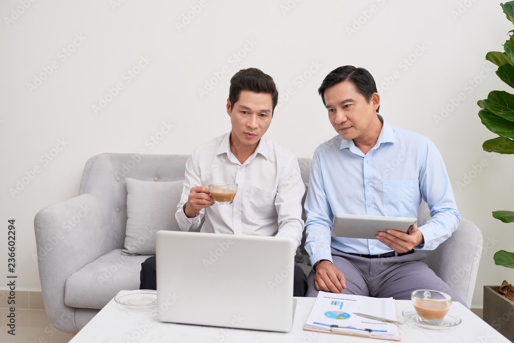 Cheerful atmosphere. Two businessman sitting in front of laptop talking about their plans.