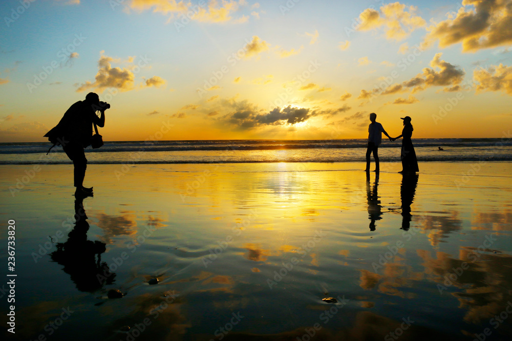 日落时分，一对浪漫情侣在海滩上散步拍照的剪影