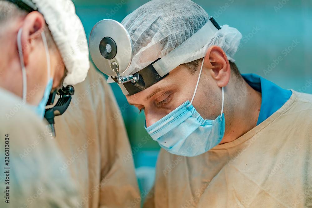 戴着口罩和放大镜的外科医生正在医院进行手术。激增