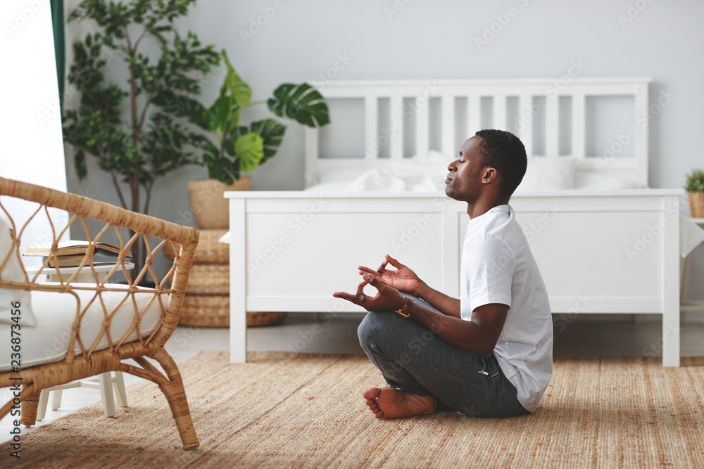 年轻黑人在家里做瑜伽，在卧室里以莲花姿势坐着