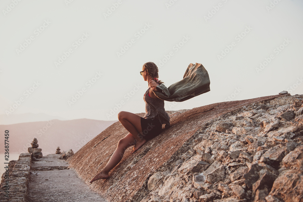年轻的女游客坐在古老的石头上，在罗兹的Monolithos城堡里眺望地平线