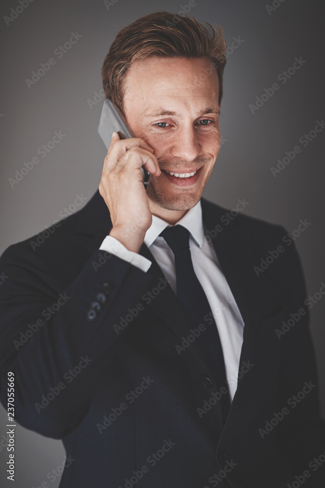 微笑的商人靠着灰色的背在手机上说话