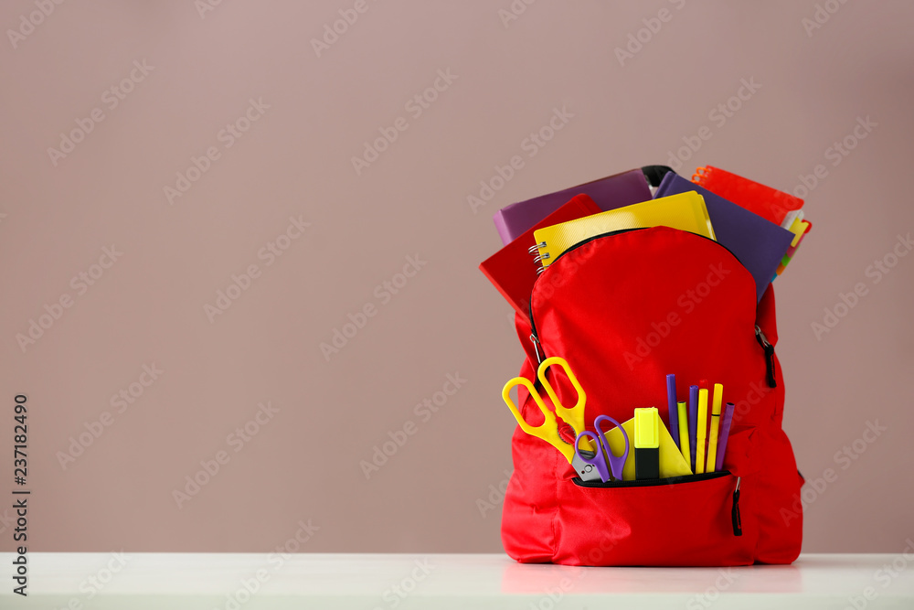 Backpack with school supplies on light table against color background