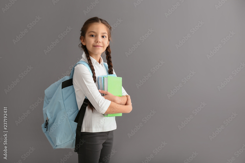 灰色背景下背着背包和书的可爱女孩