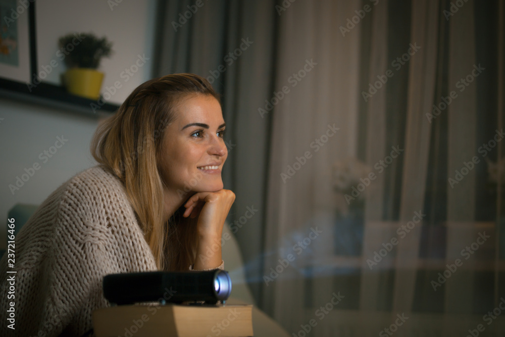 坐在沙发上的女人用数字液晶视频投影仪看电影，家庭影院