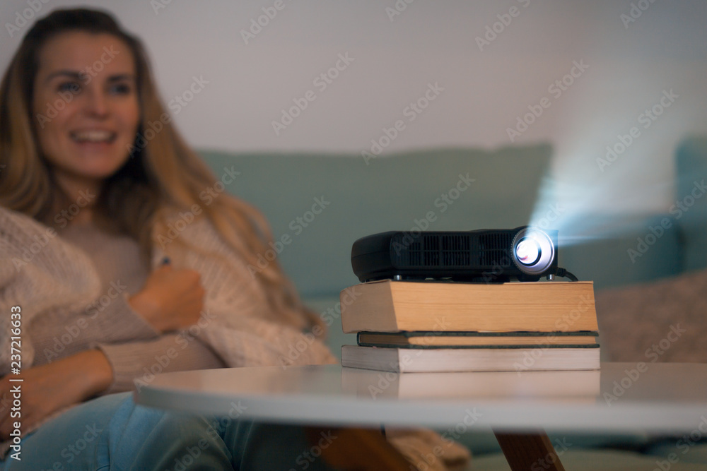 Woman on sofa watching movie using digital LCD video projector, home theater
