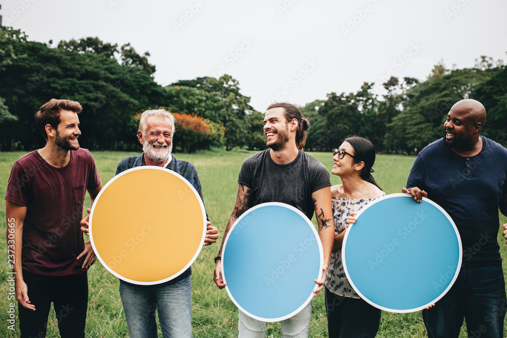 快乐的多元化人群在公园里举着圆形的空木板