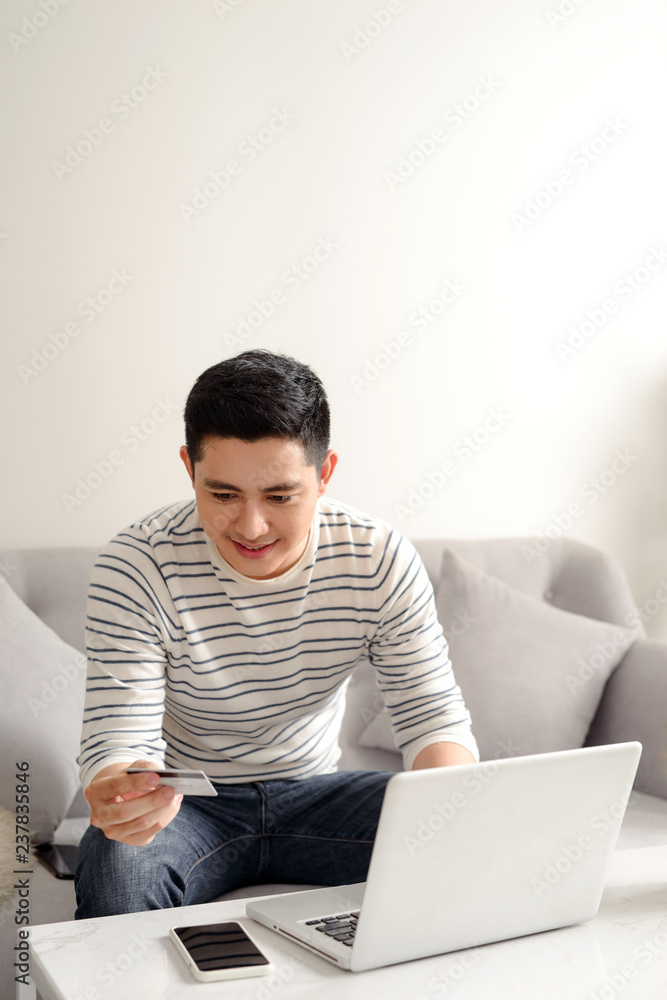 科技、人与网购理念——家里有笔记本电脑和信用卡的微笑男人