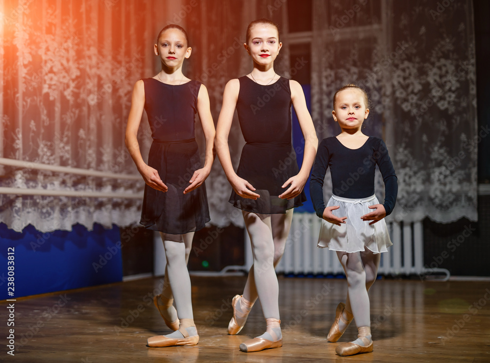 在古典舞学校里，穿着黑色西装和尖头鞋的年轻芭蕾舞演员站在同一个姿势