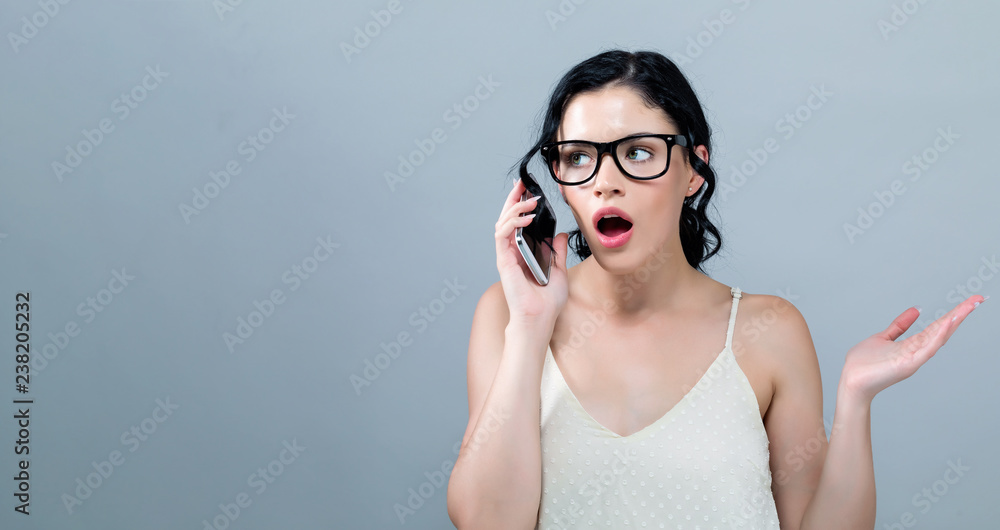 Young woman talking her the cellphone on a gray background