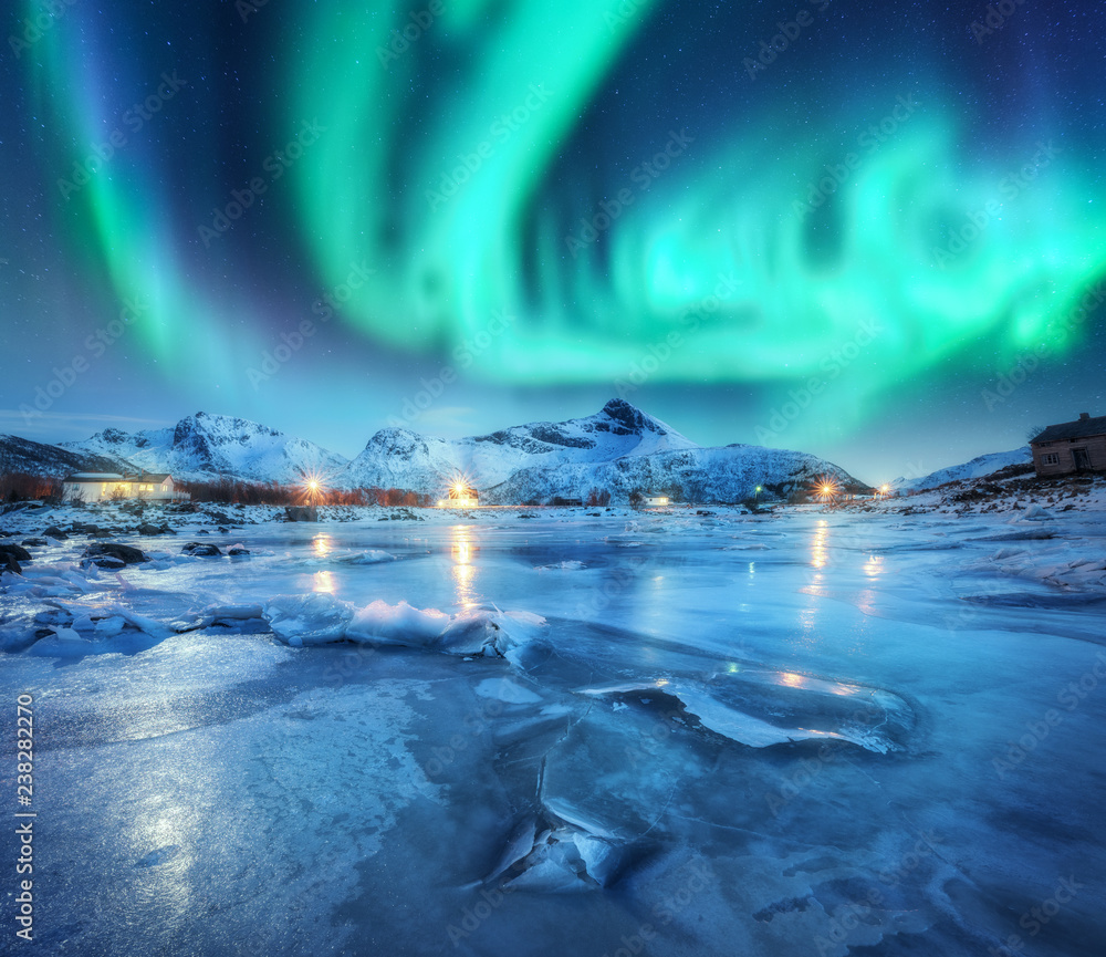 挪威罗弗敦群岛的雪山、冰冻海岸和房屋上方的北极光。极光