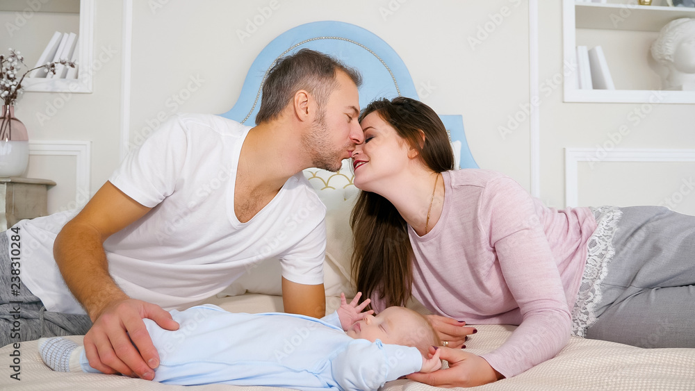漂亮的男人和女人躺在柔软的床上亲吻，靠近时尚卧室里熟睡的婴儿