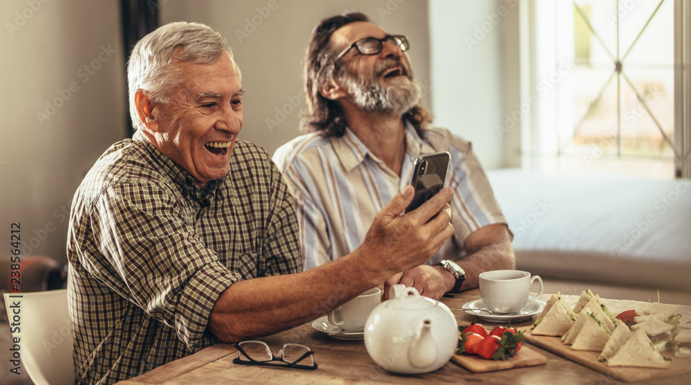 退休男子看着智能手机上的旧照片大笑