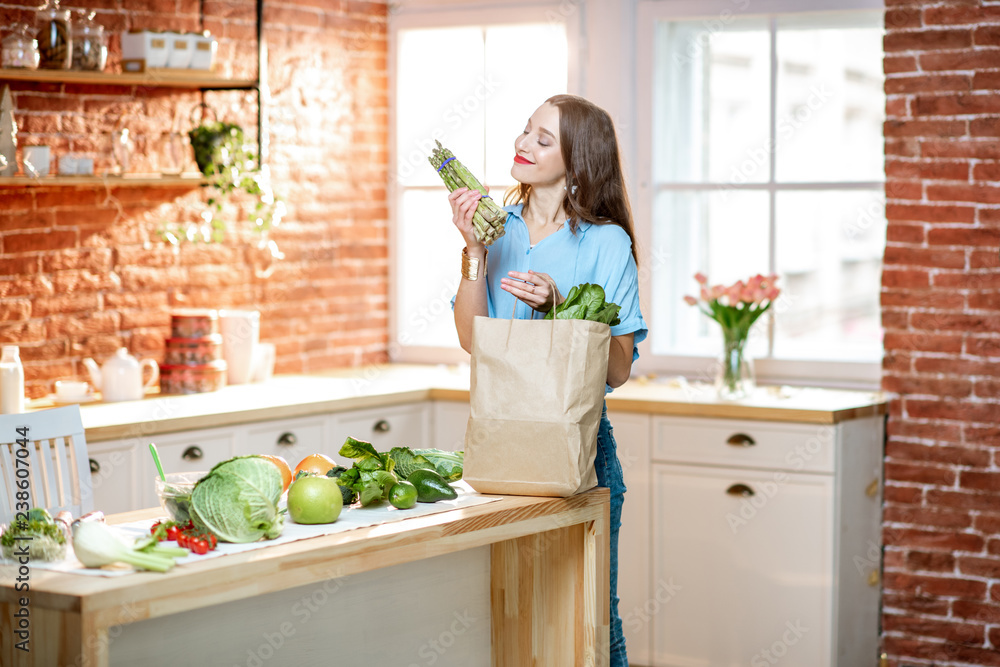 年轻女子在家厨房打开装有健康绿色蔬菜的购物袋