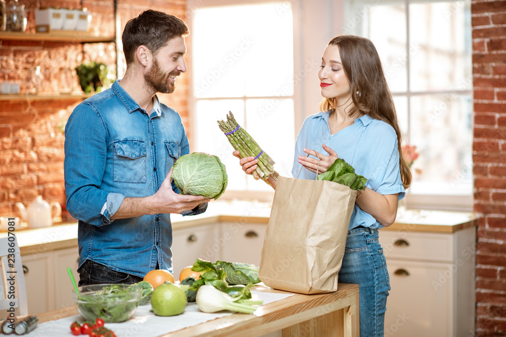 年轻的素食主义者夫妇在家里的厨房里用新鲜的绿色产品打开购物袋
