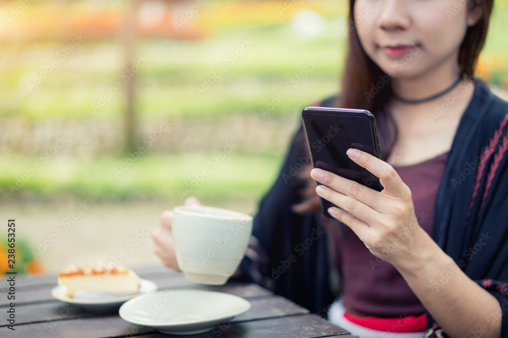 美丽的亚洲女性喜欢在花园里喝咖啡，用智能手机聊天。