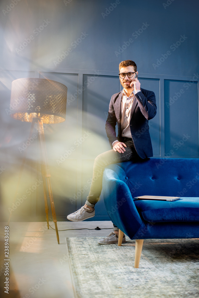一位优雅的商人的画像，他拿着笔记本电脑坐在豪华的蓝色办公室的沙发上