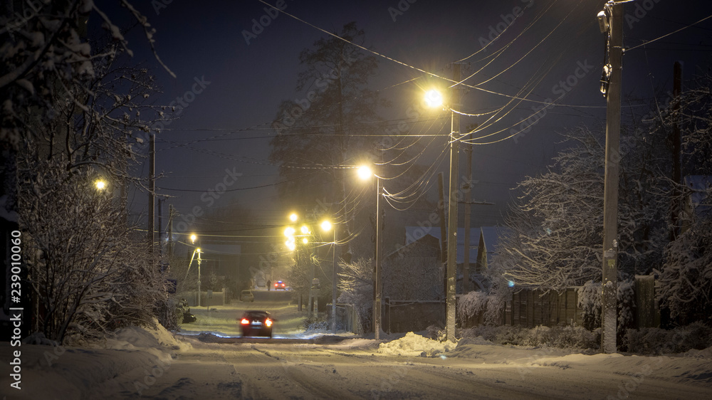 美丽的乡村冬季白雪覆盖的街道上挂着灯笼。汽车照亮了小路