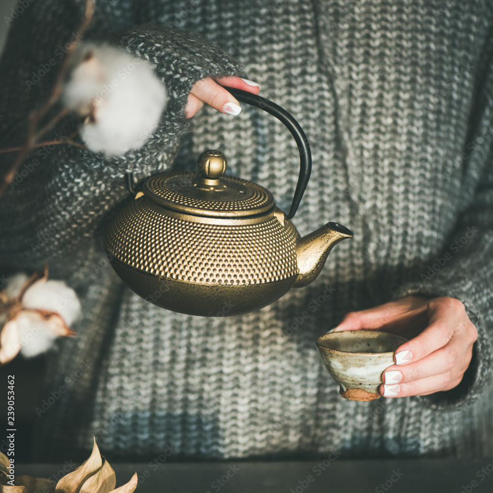茶道。穿着灰色保暖针织冬季毛衣的年轻女性从金色的铁锅里倒绿茶