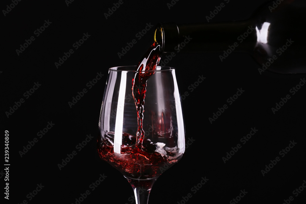 在深色背景下将红酒从瓶中倒入玻璃杯