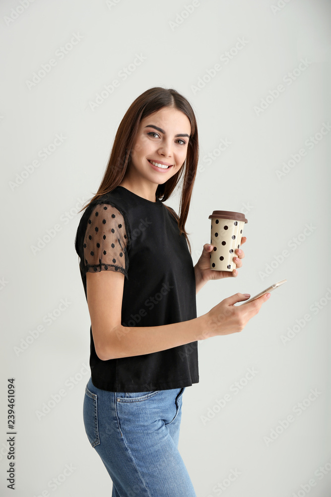 浅色背景下拿着手机和一杯咖啡的美丽女商人的肖像