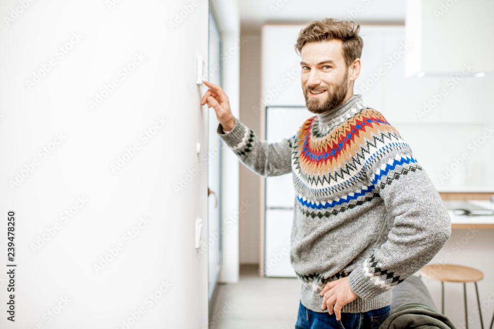 穿着毛衣的男人在家里用电子恒温器调节室温