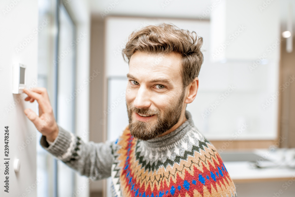 一个穿着毛衣的男人在家里用电子恒温器调节室温的肖像