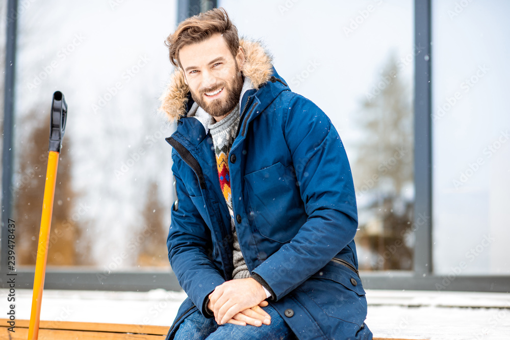 一个穿着冬装的英俊男子坐在现代房子的露台上的肖像