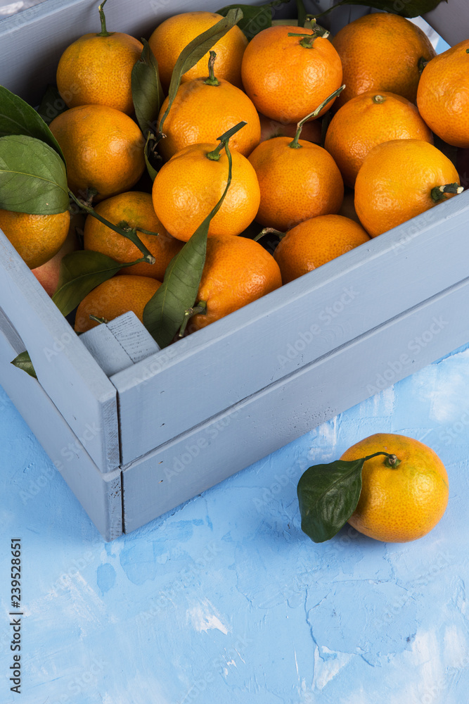 盒子里的新鲜橘子，蓝色混凝土背景上有叶子。