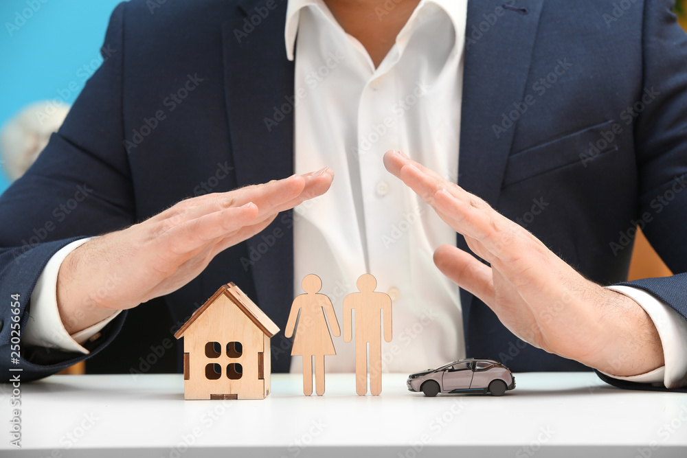 Insurance agent with toy car, human figures and house sitting at table, closeup