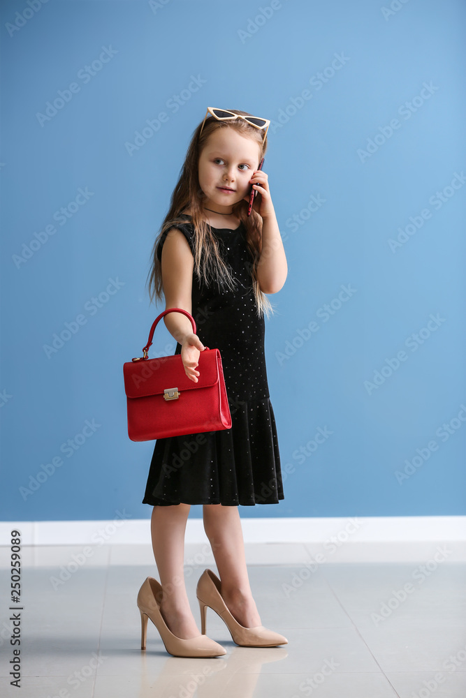穿着妈妈鞋的时尚小女孩靠着彩色墙打电话