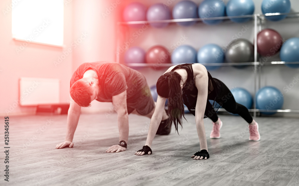 一对运动型年轻夫妇在漏光的健身房做俯卧撑。年轻女子和男子正在训练。