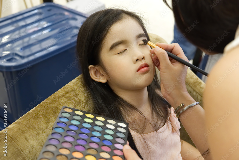 化妆专业艺术家化妆坐在椅子上刷眼睛的可爱亚洲小女孩。