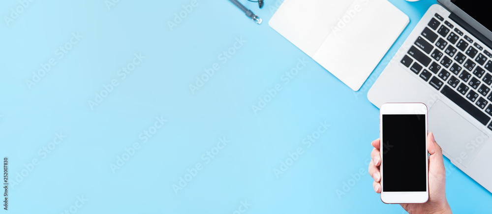 一个女人拿着一部智能手机，与一张最小的蓝色桌子隔离，这是网上购物的概念。
