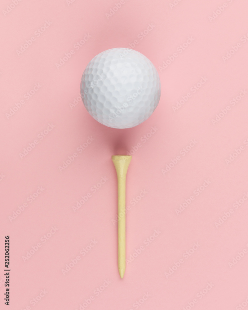 Golf ball and wooden tee on pink background closeup