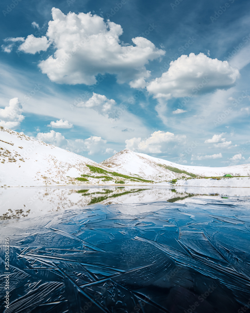结冰的山湖，湖面有蓝色的冰和裂缝。冬季雪景如画