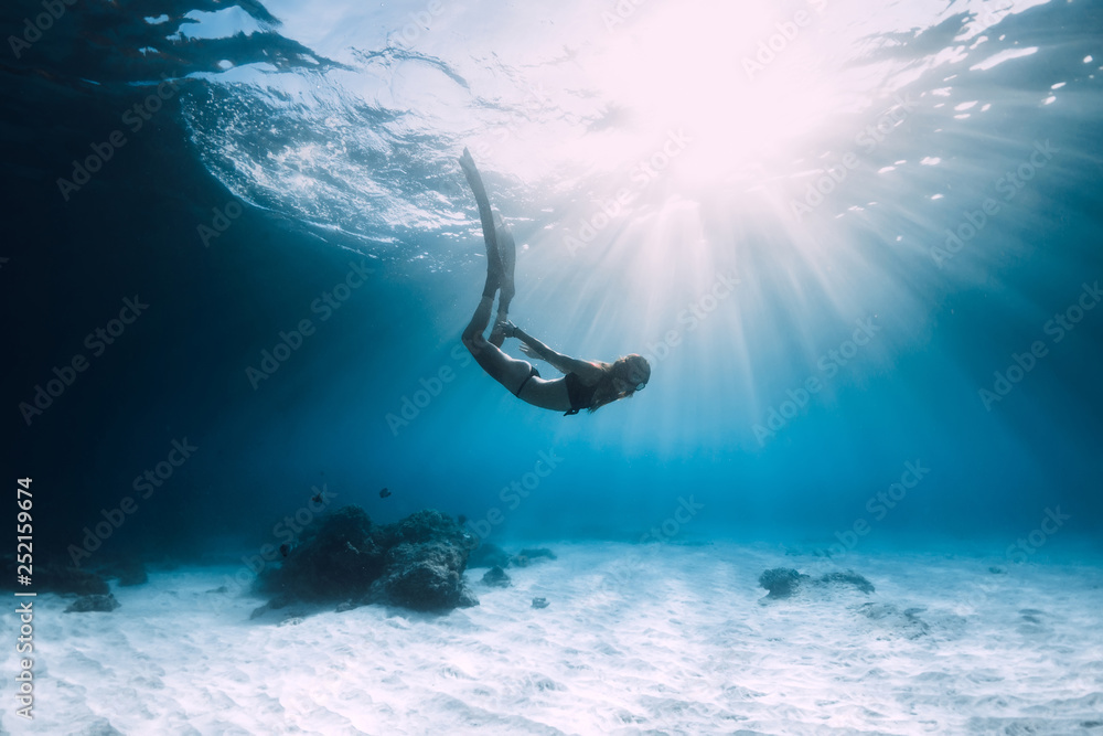 女子自由泳运动员带鳍在沙质海洋上潜水。在蓝色海洋中自由潜水