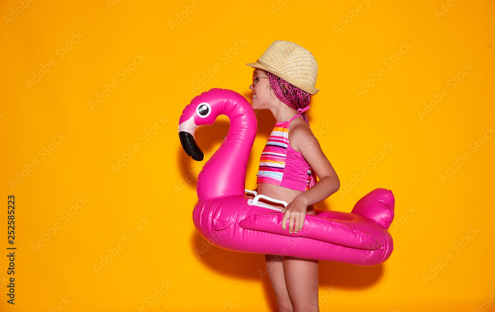 。穿着泳衣的快乐小女孩，黄色背景上有游泳圈火烈鸟。