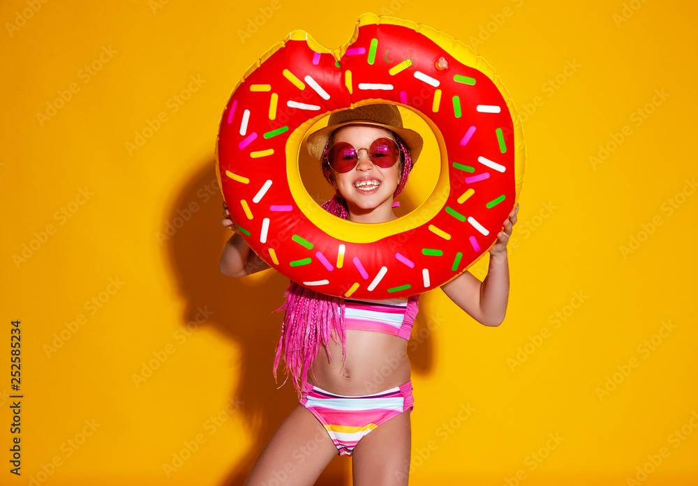 快乐的小女孩穿着黄色背景的游泳圈甜甜圈泳衣