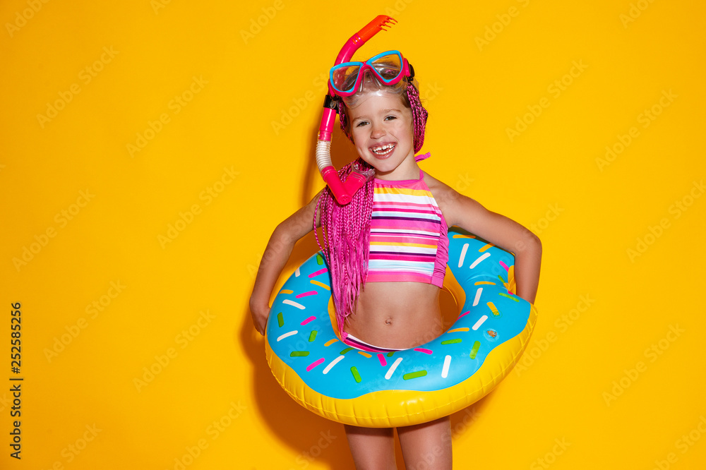 happy child girl in swimsuit with swimming ring donut on colored yellow background.