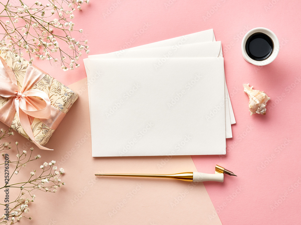 用书法笔、墨水、鲜花和礼物制作的粉红色或米色背景的空白信封模型