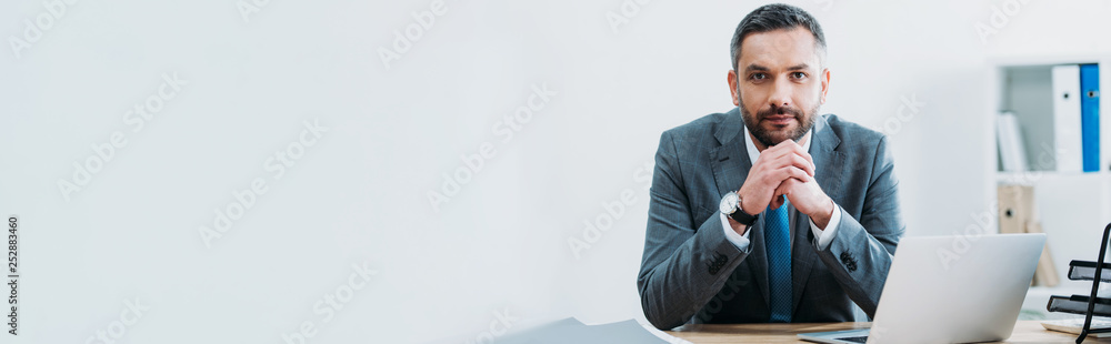 businessman sitting at table with laptop and looking at camera in office