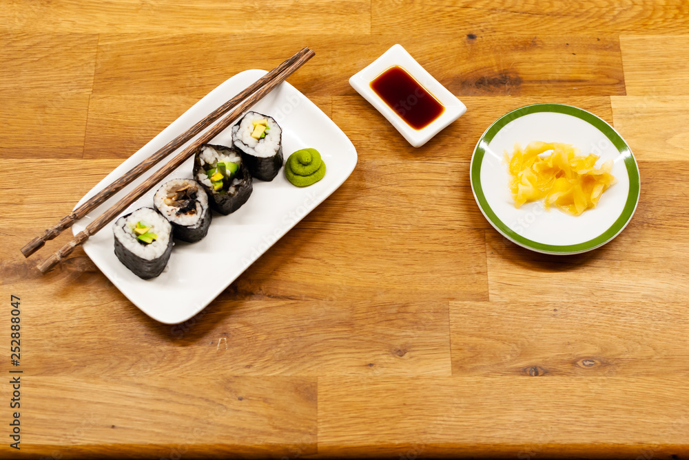 自制素食寿司卷，里面装着鳄梨，放在木桌上的一个小盘子里，里面放着酱油，哇