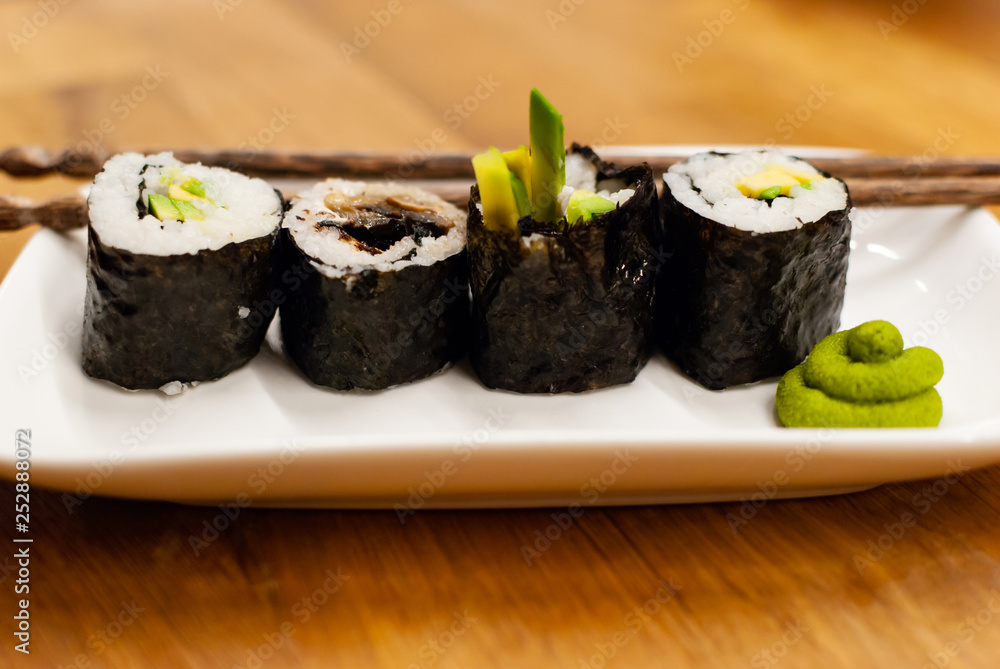 自制素食寿司卷，里面装着鳄梨，放在木桌上的一个小盘子里，放着酱油，哇